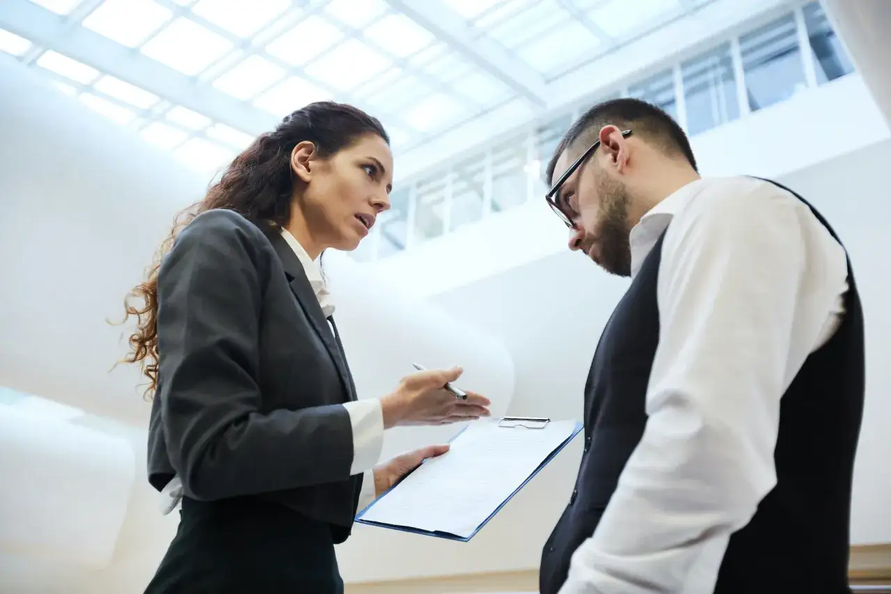 A woman explains conflict of interest policy examples from a document to a man in a modern office.