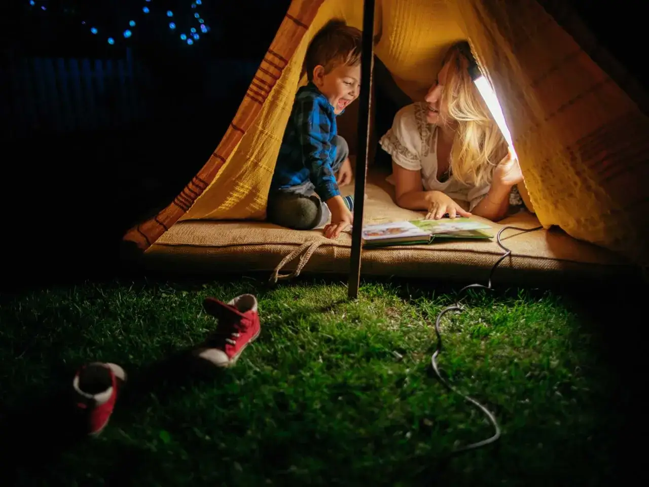 A mother and son share a magical night of reading in a backyard tent, perfect for read-a-thon ideas.