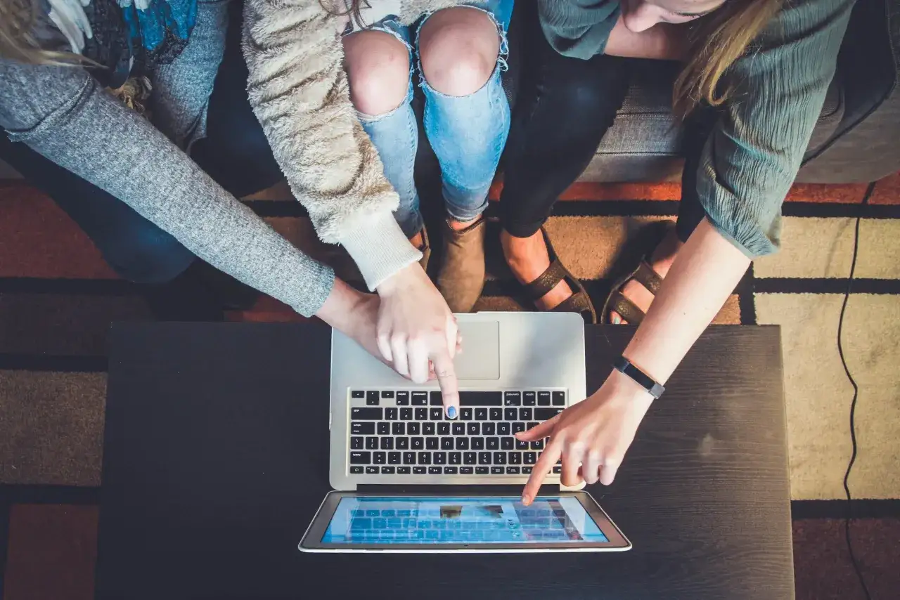 Four friends collaborate on a laptop and tablet, planning their next free online community service project.