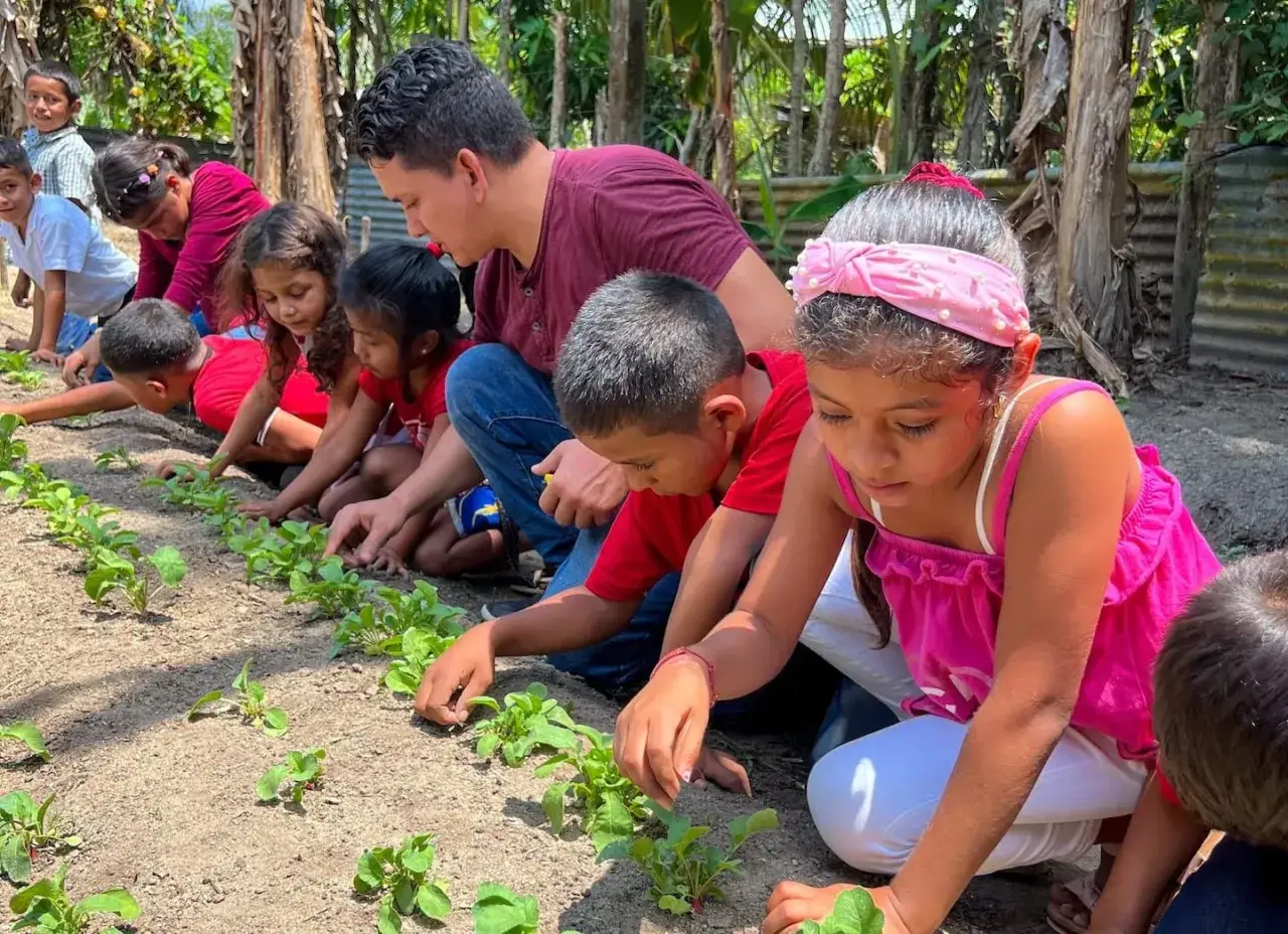 Students participate in community service projects, tending to a row of young plants in a garden.