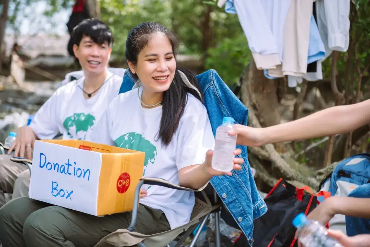 Volunteers with a donation box and water bottles, preparing for profitable fundraisers in a natural setting.